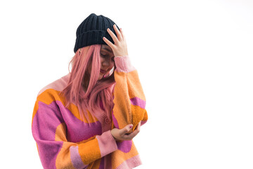 Medium closeup studio shot with white background of young caucasian pink-haired girl in black beanie and colourful cardigan toughing her forehead with one hand in a gesture of palmface. High quality