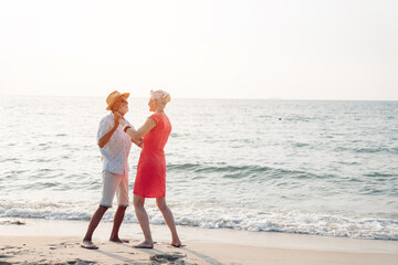 Happy senior couple in love walking and dancing together on the beach having fun in a sunny day, activity after retirement in vacations and summer.