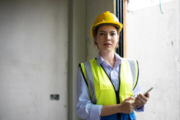 Wall Mural - Professional engineer in safety equipment at construction site. woman architect wearing hardhat at construction site while working on digital tablet.