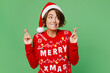 © ViDi Studio - Merry young woman wear xmas sweater Santa hat posing wait for special moment keep fingers crossed look aside isolated on plain pastel light green background. Happy New Year 2023 celebration concept.