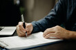 © khunkornStudio - Businessman signs documents with a pen making the signature contract and partnership on desk.