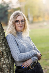 Portrait of beautiful young woman in glasses posing leaning against a autumn tree. Vertically.