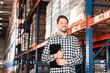 © New Africa - Happy manager holding clipboard in warehouse with lots of products, low angle view