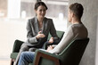 © fizkes - Two colleagues having good friendly conversation, talking seated on armchairs meet in office lobby, during break at workday. Businesspeople, partners solve business, share solutions and ideas indoors