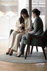 Middle-aged and millennial businesswomen laughing during meeting in office, discuss on-line project using digital tablet device, having fun during break looking cheerful enjoy modern tech app and talk