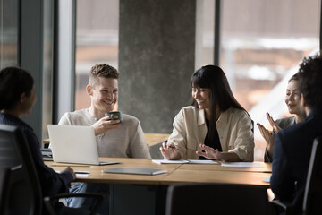 Canvas Print - Group of smiling colleagues sit at table gathered in modern boardroom, brainstorm, discuss project joking and laughing, having fun, cooperating together at office meeting. Teamwork, break, friendship