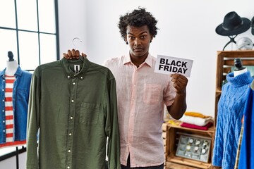 Sticker - African man with curly hair holding black friday banner at retail shop clueless and confused expression. doubt concept.