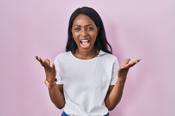 Poster - African young woman wearing casual white t shirt crazy and mad shouting and yelling with aggressive expression and arms raised. frustration concept.