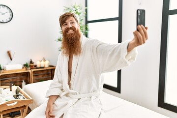 Wall Mural - Young redhead man wearing bathrobe make selfie by the smartphone at beauty center