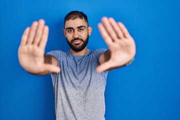 Poster - Middle east man with beard standing over blue background doing frame using hands palms and fingers, camera perspective