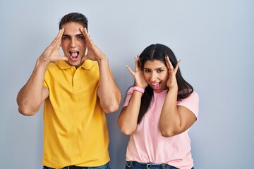 Canvas Print - Young couple standing over isolated background smiling cheerful playing peek a boo with hands showing face. surprised and exited