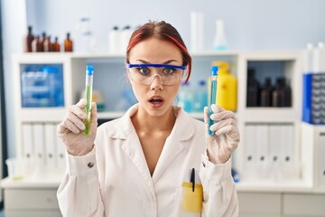 Poster - Young caucasian woman working at scientist laboratory holding samples afraid and shocked with surprise and amazed expression, fear and excited face.