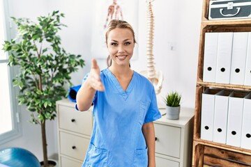 Canvas Print - Young caucasian woman working at pain recovery clinic smiling friendly offering handshake as greeting and welcoming. successful business.