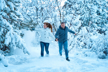 Wall Mural - A young couple in love fooling around in the winter woods playing and throwing snow at each other