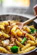 woman hand cooking tasty chicken fillet with mushroom in a creamy sauce with fusilli pasta in pan on kitchen