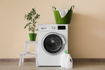 Canvas Print - Washing machine with laundry basket, houseplant on stepladder and detergent near beige wall