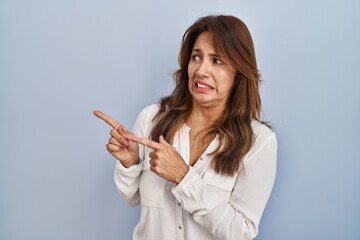 Sticker - Hispanic woman standing over isolated background pointing aside worried and nervous with both hands, concerned and surprised expression