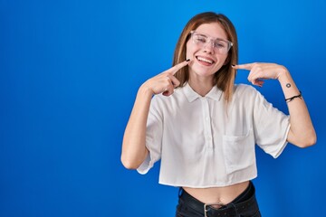 Sticker - Beautiful woman standing over blue background smiling cheerful showing and pointing with fingers teeth and mouth. dental health concept.