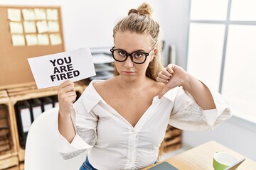 Sticker - Young caucasian woman holding you are fired banner at the office with angry face, negative sign showing dislike with thumbs down, rejection concept