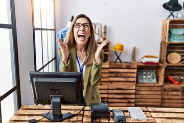 Wall Mural - Young hispanic woman working as manager at retail boutique celebrating mad and crazy for success with arms raised and closed eyes screaming excited. winner concept