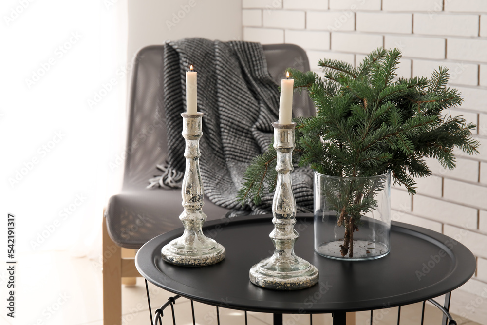 Vase with Christmas branches and candles on table in light living room