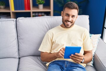 Poster - Young hispanic man using touchpad sitting on sofa at home