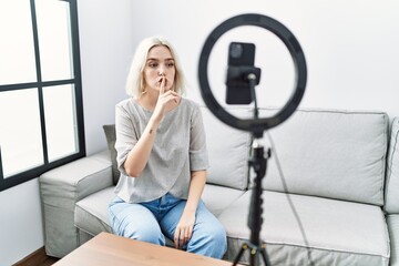 Poster - Young caucasian woman recording vlog tutorial with smartphone at home asking to be quiet with finger on lips. silence and secret concept.