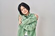 © Krakenimages.com - Young asian woman standing over white background hugging oneself happy and positive, smiling confident. self love and self care