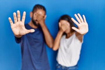 Canvas Print - Young hispanic couple standing together covering eyes with hands and doing stop gesture with sad and fear expression. embarrassed and negative concept.