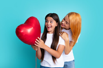 Poster - Mothers day. Smiling mother and daughter holding love heart balloon on blue background. Mommy with teenager daughter isolated on blue background studio portrait. Love family, parenthood concept.