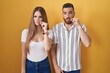 © Krakenimages.com - Young couple standing over yellow background mouth and lips shut as zip with fingers. secret and silent, taboo talking