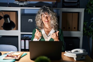 Sticker - Middle age woman working at night using computer laptop doing money gesture with hands, asking for salary payment, millionaire business