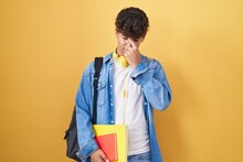 Hispanic Teenager Wearing Student Backpack And Holding Books Tired Rubbing Nose And Eyes Feeling Fatigue And Headache. Stress And Frustration Concept.