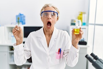 Poster - Middle age blonde woman working at laboratory in shock face, looking skeptical and sarcastic, surprised with open mouth