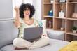 © Krakenimages.com - Young brunette woman with curly hair using laptop sitting on the sofa at home angry and mad raising fist frustrated and furious while shouting with anger. rage and aggressive concept.