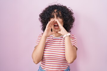 Sticker - Young middle east woman standing over pink background shouting angry out loud with hands over mouth