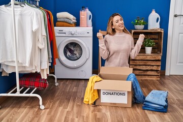 Poster - Hispanic woman putting clothes in donation box very happy and excited doing winner gesture with arms raised, smiling and screaming for success. celebration concept.