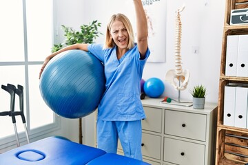 Wall Mural - Young caucasian physiotherapist woman holding pilates ball annoyed and frustrated shouting with anger, yelling crazy with anger and hand raised