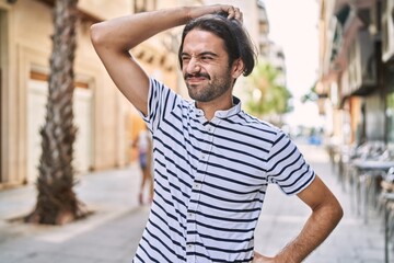 Wall Mural - Young hispanic man with beard outdoors at the city confuse and wonder about question. uncertain with doubt, thinking with hand on head. pensive concept.