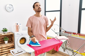 Sticker - Young hispanic man ironing clothes at home crazy and mad shouting and yelling with aggressive expression and arms raised. frustration concept.