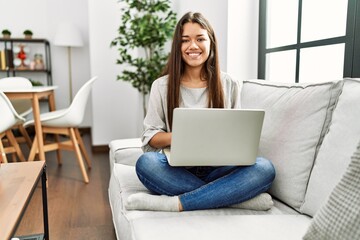 Wall Mural - Young latin woman using laptop sitting on sofa at home
