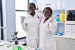 © Krakenimages.com - Two african women working at scientist laboratory pointing thumb up to the side smiling happy with open mouth