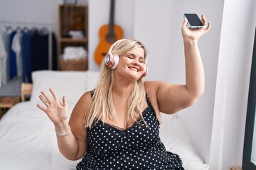 Sticker - Young woman sitting on bed listening to music and dancing at bedroom