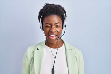 Wall Mural - African american woman wearing call center agent headset winking looking at the camera with sexy expression, cheerful and happy face.