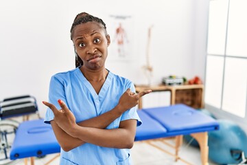 Wall Mural - Black woman with braids working at pain recovery clinic pointing to both sides with fingers, different direction disagree