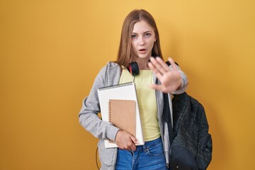 Canvas Print - Young caucasian woman wearing student backpack and holding books doing stop gesture with hands palms, angry and frustration expression