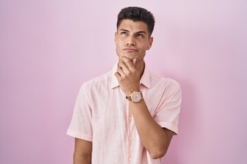 Sticker - Young hispanic man standing over pink background thinking concentrated about doubt with finger on chin and looking up wondering