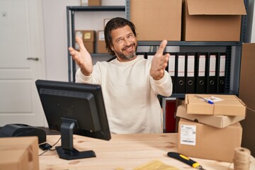 Poster - Handsome middle age man working at small business ecommerce looking at the camera smiling with open arms for hug. cheerful expression embracing happiness.