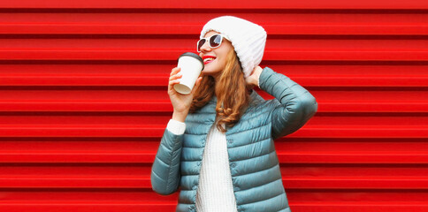 Wall Mural - Portrait of happy smiling young woman with cup of coffee wearing white hat on red background