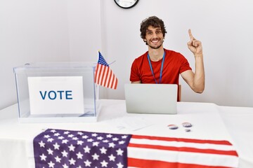 Sticker - Young hispanic man at political election sitting by ballot showing and pointing up with finger number one while smiling confident and happy.